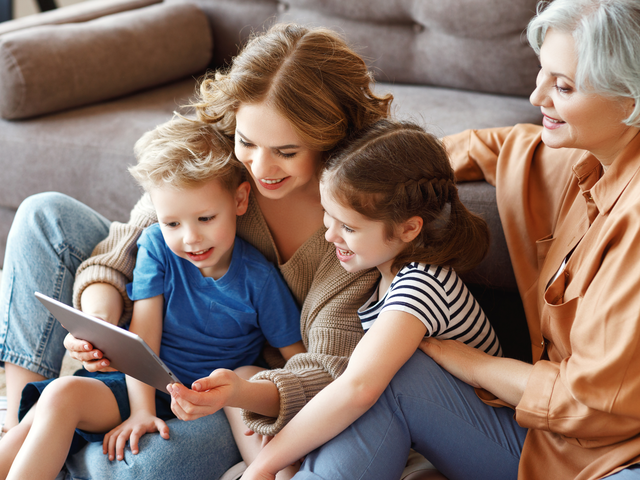 Frau sitzt mit zwei Kindern und einer älteren Person auf dem Sofa
