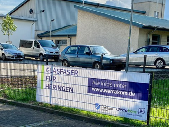 Banner hängt an einem Zaun, im Hintergrund sind Häuser und eine Straße