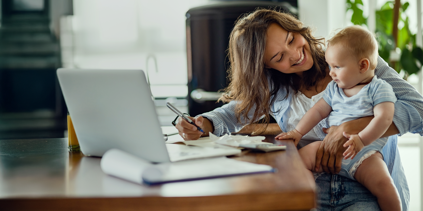 Eine Frau mit einem Kleinkind auf dem Schoß nutzt ihren Laptop im Homeoffice. Das Bild steht symbolisch für die Vereinbarkeit von Familie, Beruf und digitaler Zukunft dank zuverlässiger Glasfaseranbindung.
