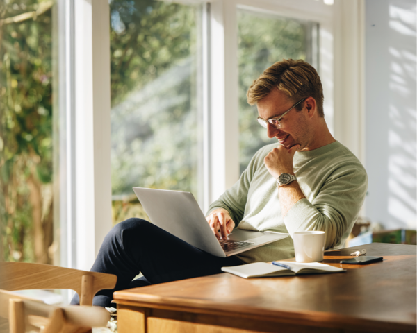Ein Mann arbeitet mit einem Laptop entspannt am Fenster – Symbolbild für stabiles Internet im Homeoffice