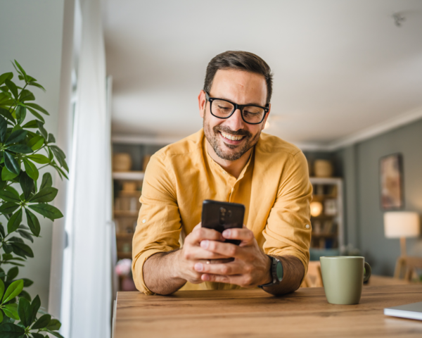 Mann lehnt sich auf den Tisch und bedient ein Handy