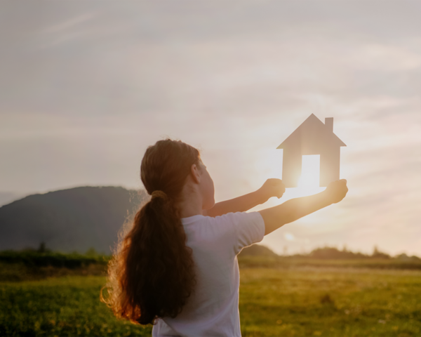 Kind hält symbolisch ein Haus in den Sonnenuntergang – Sinnbild für Zukunft und Hausbau