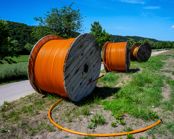 Große Glasfaserkabeltrommeln liegen entlang eines Weges im Grünen.