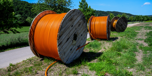 Große Glasfaserkabeltrommeln liegen entlang eines Weges im Grünen.