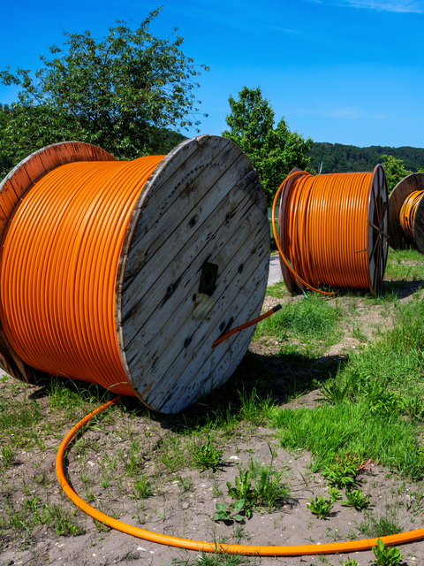 Große Glasfaserkabeltrommeln liegen entlang eines Weges im Grünen.