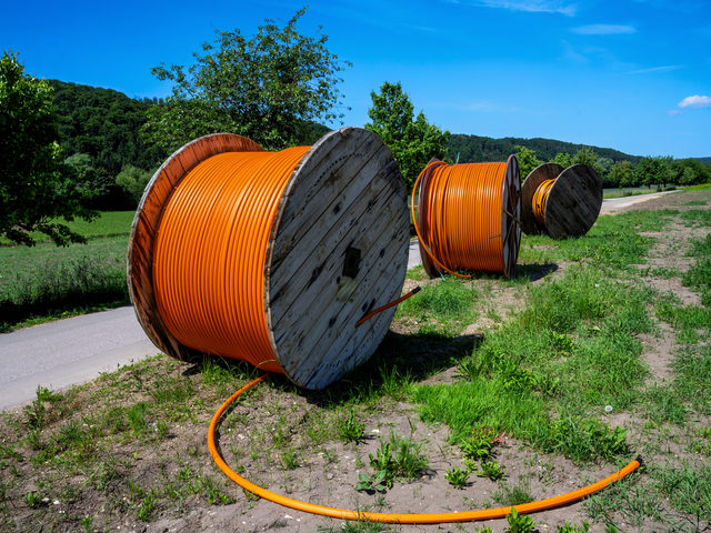 Große Glasfaserkabeltrommeln liegen entlang eines Weges im Grünen.