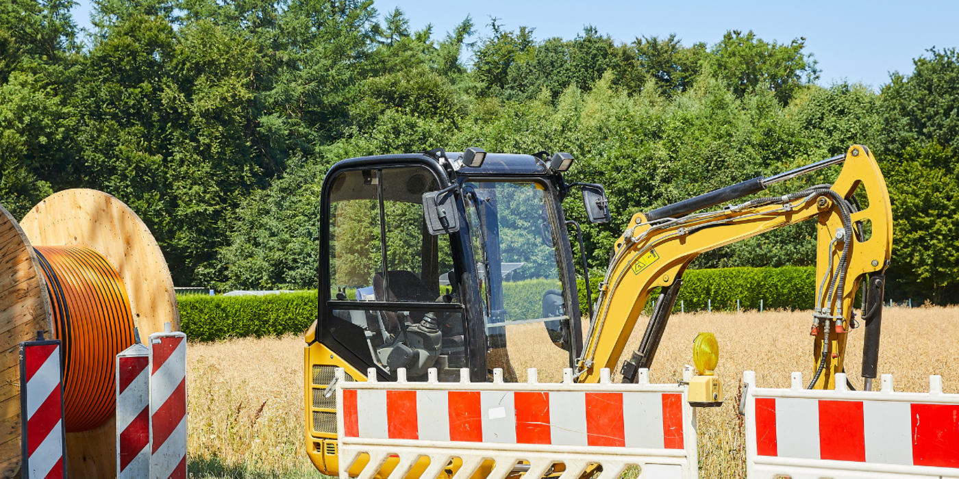 Bagger steht am Straßenrand, ein Feld ist im Hintergrund