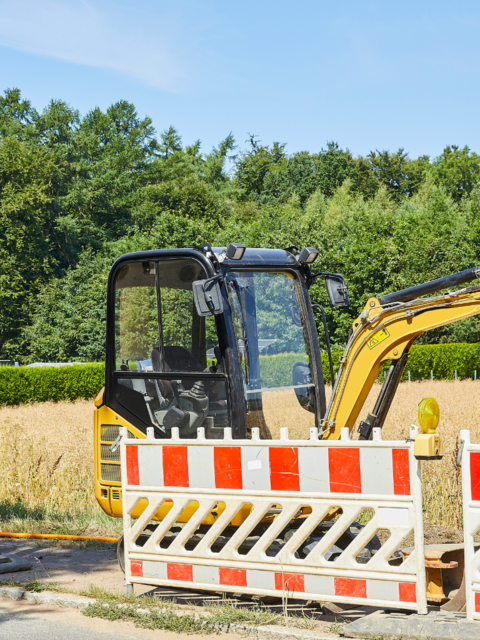 Bagger steht am Straßenrand, ein Feld ist im Hintergrund
