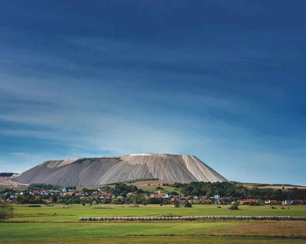 Eine Ortschaft liegt inmitten grüner Felder vor einem markanten großen Berg.