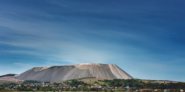 Eine Ortschaft liegt inmitten grüner Felder vor einem markanten großen Berg.
