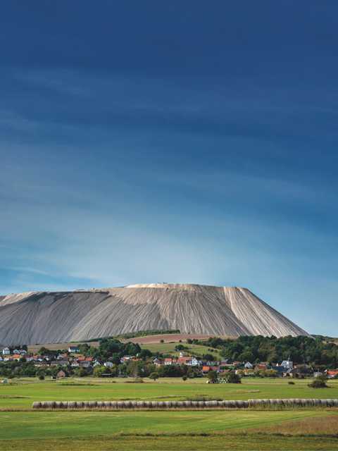 Eine Ortschaft liegt inmitten grüner Felder vor einem markanten großen Berg.