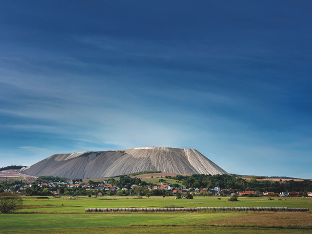 Eine Ortschaft liegt inmitten grüner Felder vor einem markanten großen Berg.